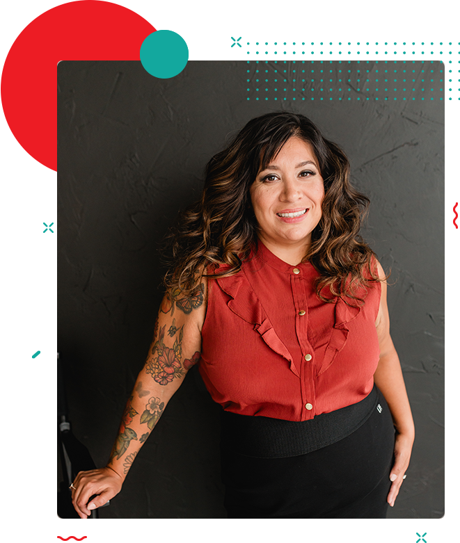 A woman with long, wavy hair and arm tattoos is smiling. She is wearing a sleeveless red blouse and leaning against a dark wall. Decorative shapes are overlaid on the image, evoking a sense of home and comfort.